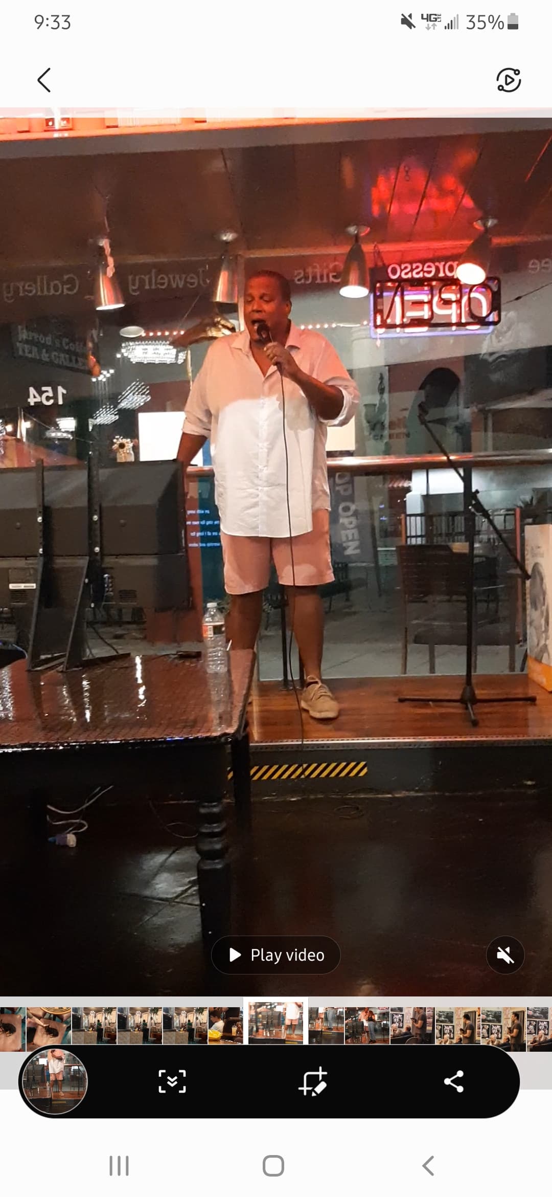 Man in a white shirt and pink shorts sings into a microphone on stage.