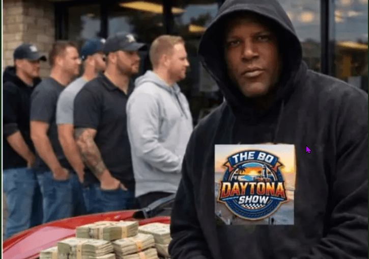 Man in black hoodie stands near stacks of cash with men lined up behind him.